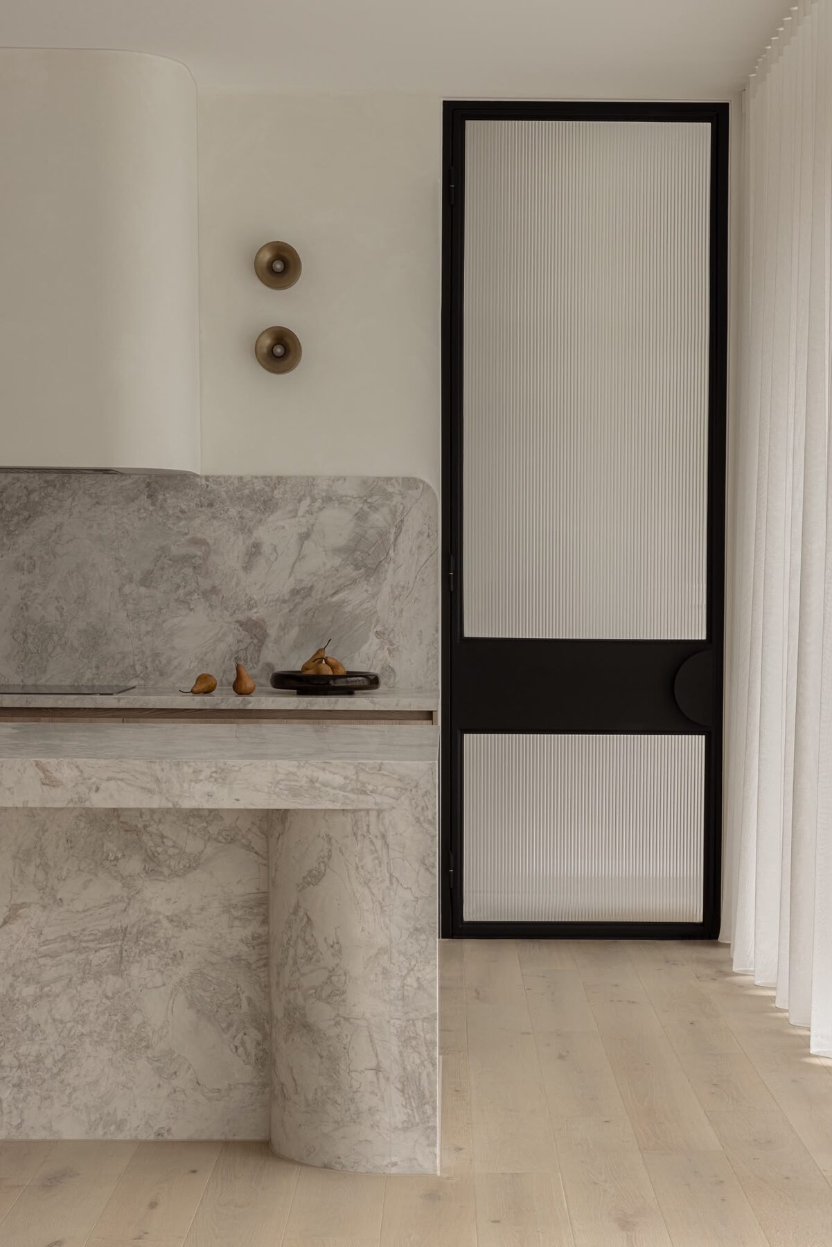 Alphington Residence — curved stone kitchen island beside a fluted glass door